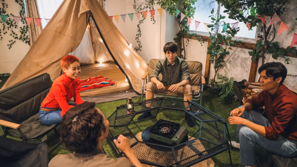 A group of friends gathering around a portable stove and a tent in a living room setup, showing that camping can also be done indoors for a unique social experience.