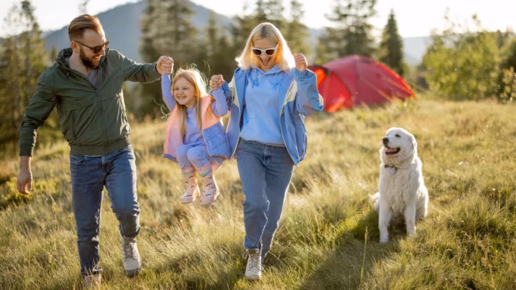 A family with a child and a dog playing in a grassy meadow near their tent, illustrating why camping is the best outdoor activity for building strong bonds and enjoying nature.