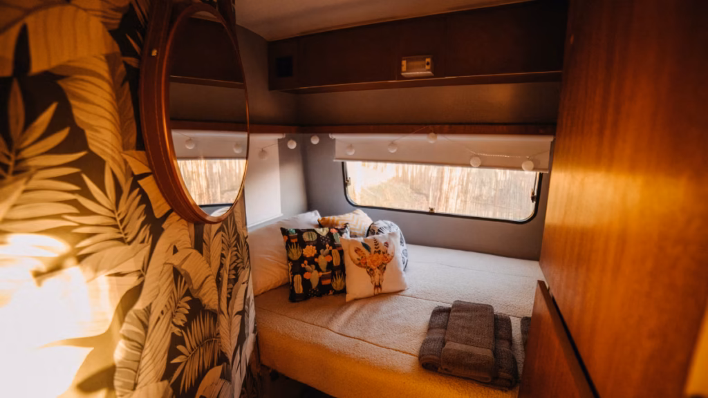 Cozy camper van interior with a made bed, warm wood paneling, and natural window light answering the question can you live in a camper year-round with a comfortable full-time home setup.