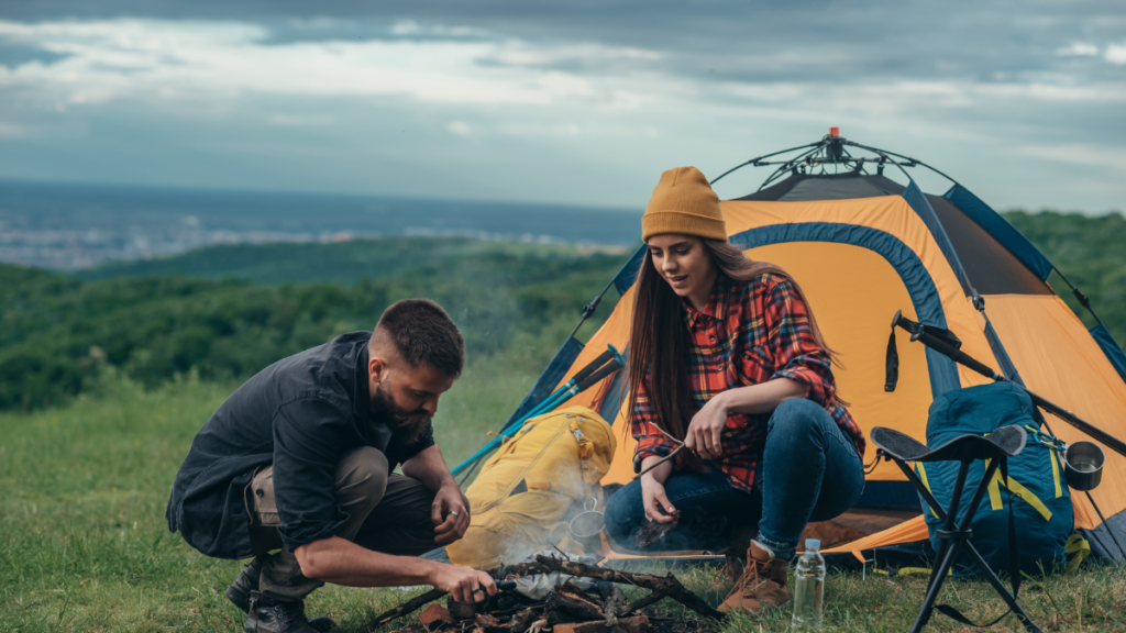 Adult camper sitting beside a fire whittling a green wood spoon, demonstrating crafts to do while camping for adults.