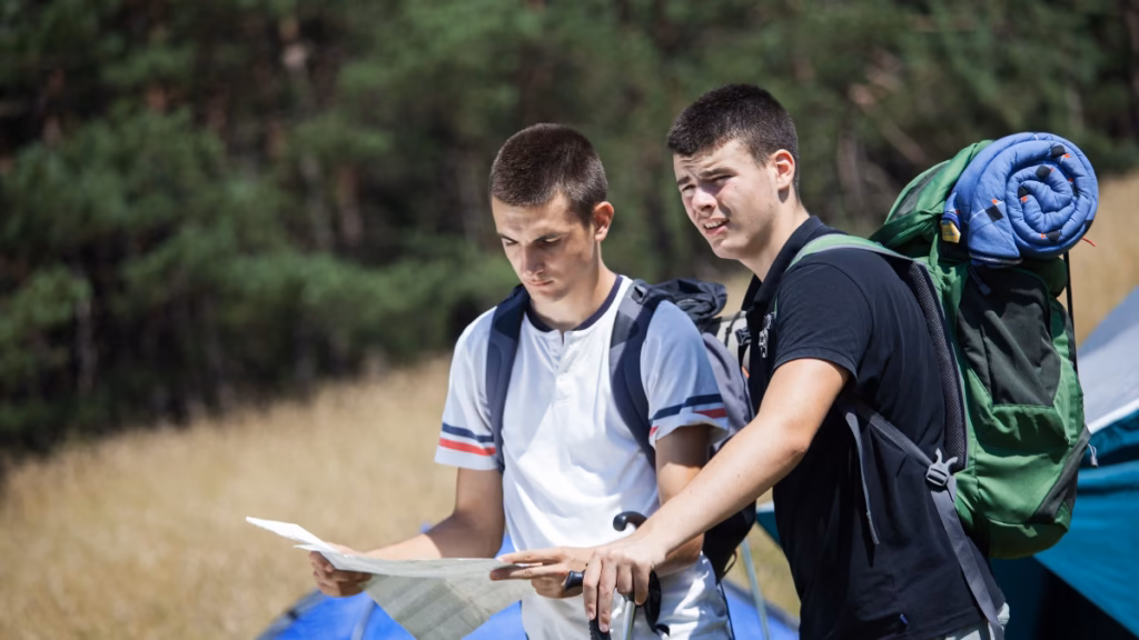 Two teenage boys reading a map at a wilderness camp, representing summer camps in America for 16-year-olds focused on outdoor adventure and self-reliance.